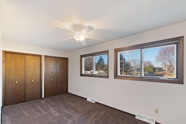 unfurnished bedroom featuring visible vents, multiple closets, a textured ceiling, and dark carpet