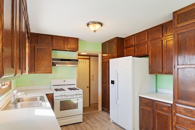 kitchen featuring light wood finished floors, under cabinet range hood, light countertops, white appliances, and a sink