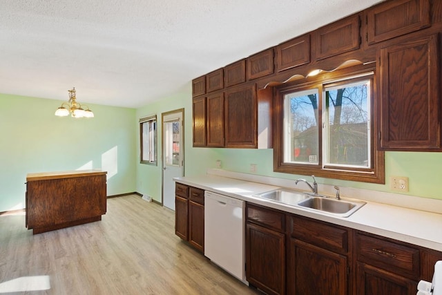 kitchen with a sink, light wood-type flooring, white dishwasher, and light countertops