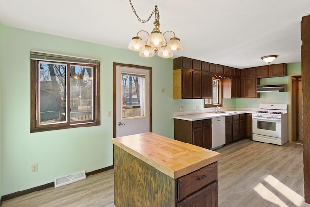 kitchen featuring white appliances, visible vents, light wood-style flooring, a sink, and under cabinet range hood