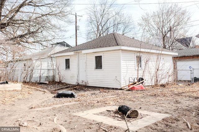 back of house featuring an outbuilding, a shingled roof, and fence