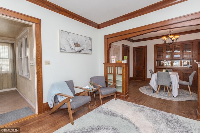 living area featuring crown molding, wood finished floors, baseboards, and a chandelier