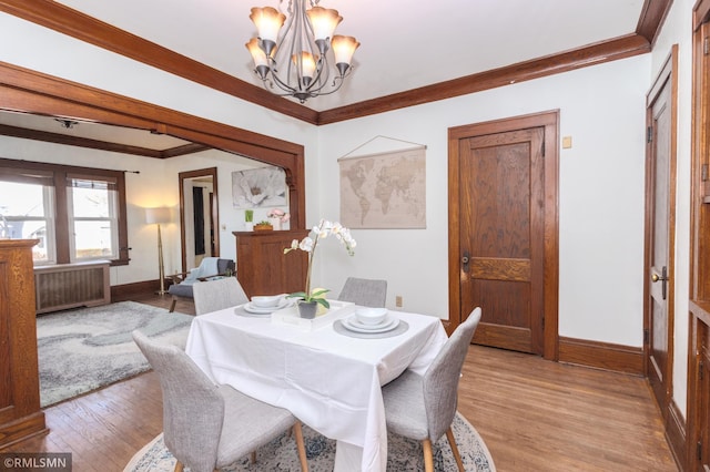 dining area with an inviting chandelier, radiator, light wood finished floors, and ornamental molding