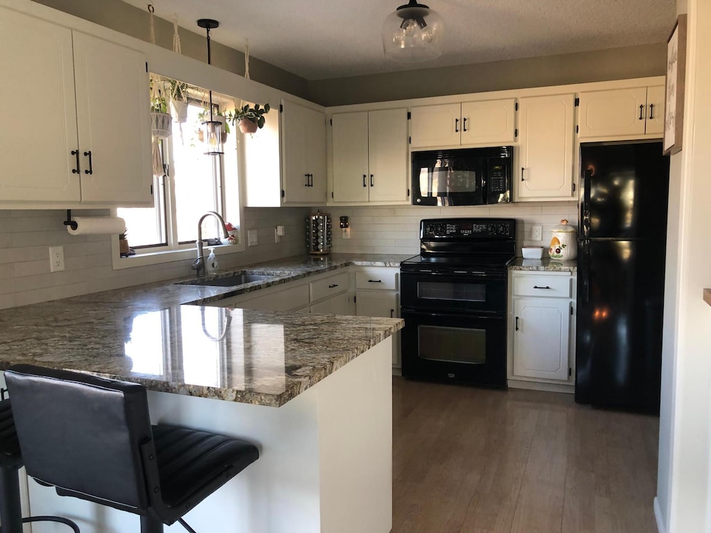 kitchen featuring white cabinetry, black appliances, a peninsula, and a sink