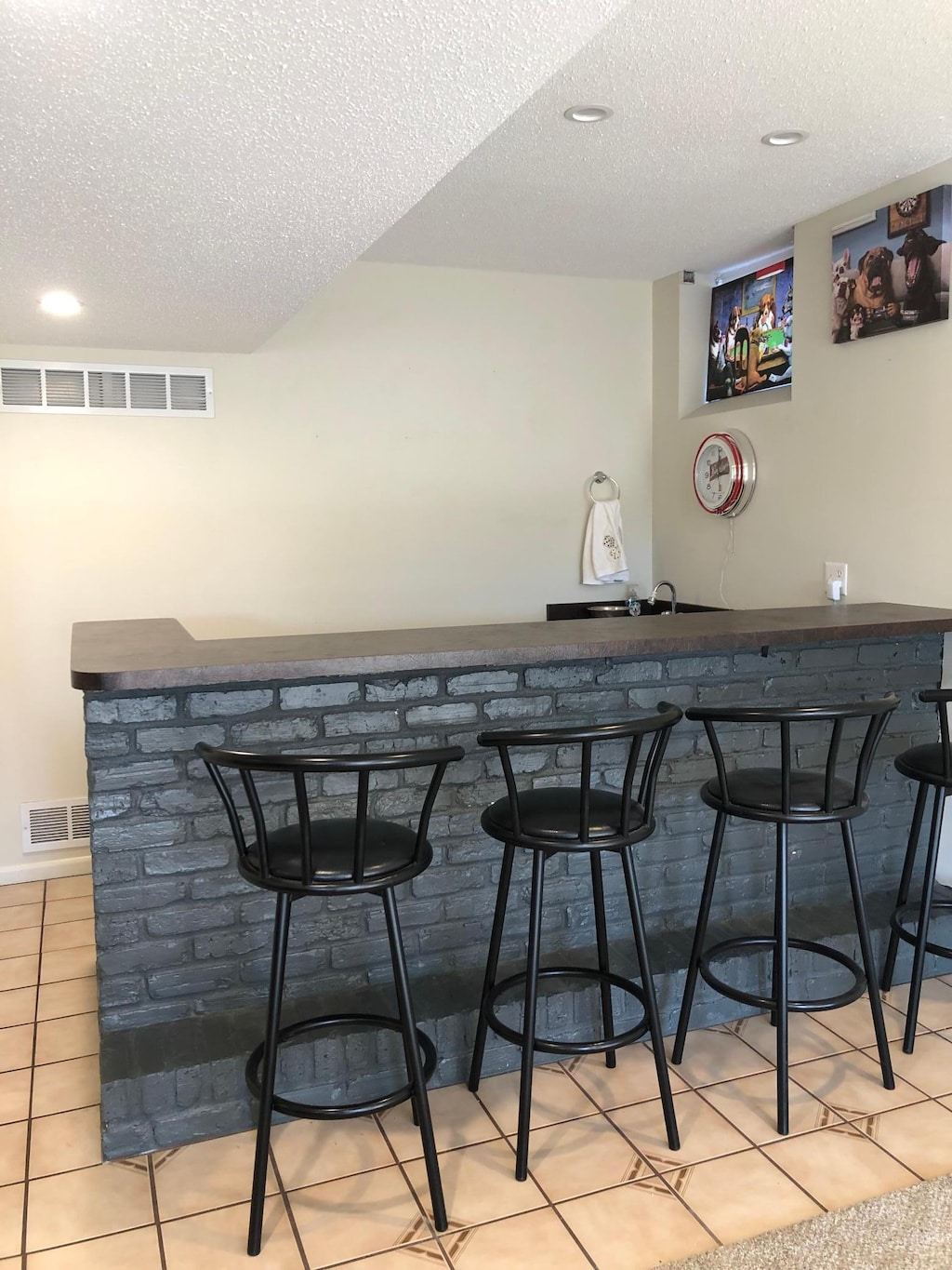 bar featuring tile patterned floors, visible vents, a textured ceiling, and indoor wet bar