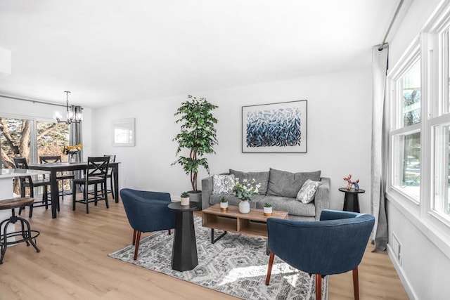 living area featuring a notable chandelier, a healthy amount of sunlight, baseboards, and light wood-style floors