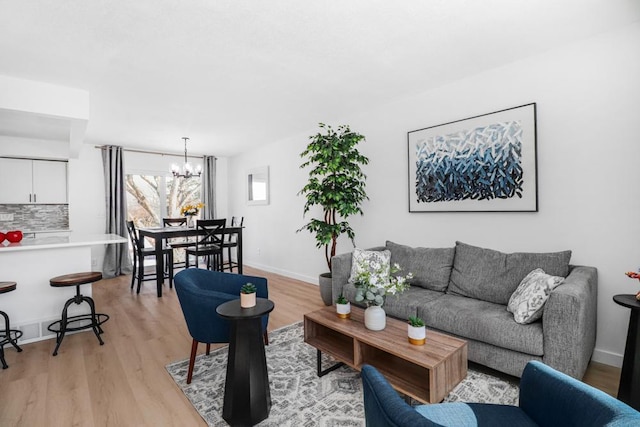 living area with light wood-type flooring, baseboards, and an inviting chandelier