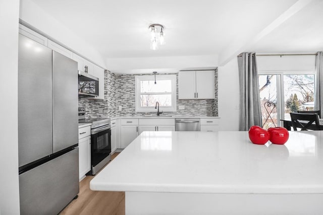 kitchen featuring light countertops, decorative backsplash, stainless steel appliances, white cabinetry, and a sink