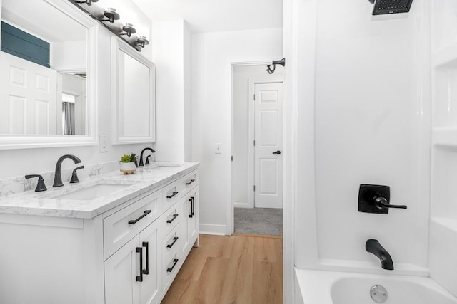 bathroom with double vanity, shower / tub combination, wood finished floors, and a sink