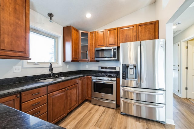 kitchen with a sink, lofted ceiling, light wood finished floors, and stainless steel appliances