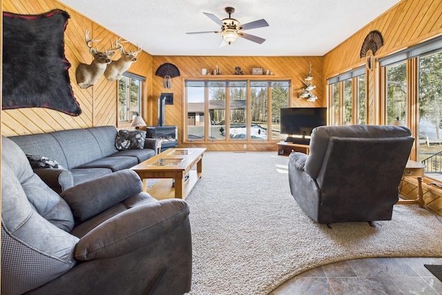 living area featuring plenty of natural light, wood walls, a wood stove, and a ceiling fan