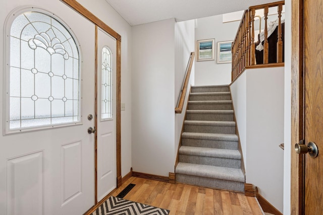 foyer featuring baseboards, light wood-style floors, and stairs