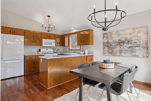 kitchen with dark wood finished floors, lofted ceiling, brown cabinets, an inviting chandelier, and white appliances