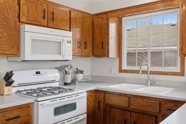 kitchen featuring a sink, white appliances, brown cabinets, and light countertops