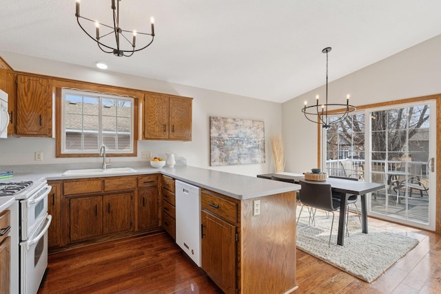 kitchen with lofted ceiling, a peninsula, an inviting chandelier, white appliances, and a sink