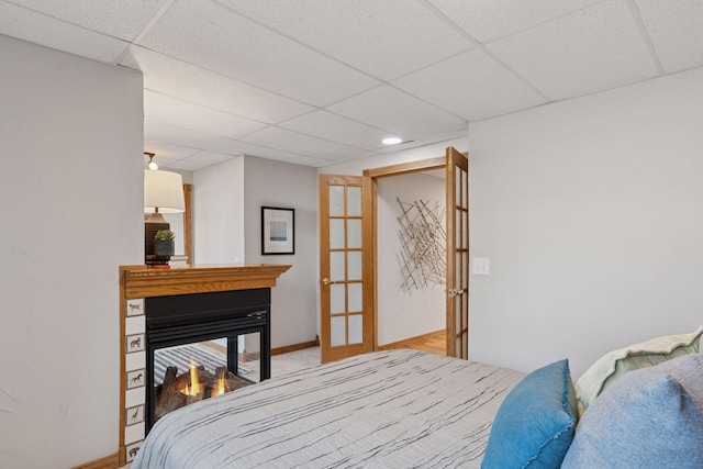 bedroom with baseboards, french doors, a multi sided fireplace, and a paneled ceiling