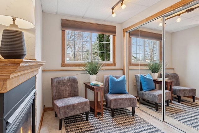 sitting room with light tile patterned flooring, rail lighting, baseboards, and a lit fireplace