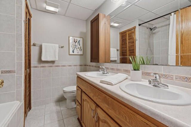 bathroom with tile walls, toilet, tile patterned floors, and a sink