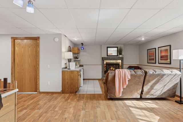 living room featuring a glass covered fireplace, light wood-type flooring, baseboards, and a drop ceiling