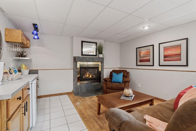 living area with a tiled fireplace, a paneled ceiling, baseboards, and light wood finished floors