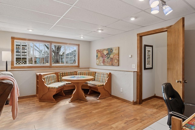 dining space featuring light wood-style floors, baseboards, and a drop ceiling