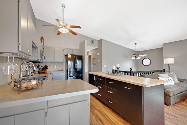 kitchen with a ceiling fan, light wood finished floors, lofted ceiling, freestanding refrigerator, and backsplash