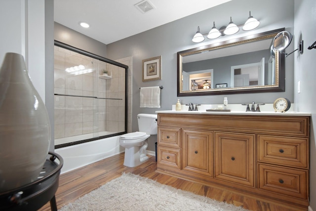 bathroom featuring vanity, wood finished floors, visible vents, enclosed tub / shower combo, and toilet