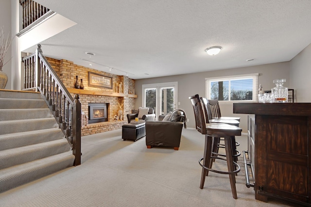 living area with a textured ceiling, carpet floors, a brick fireplace, a dry bar, and stairs