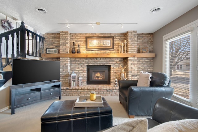 living area featuring visible vents, a textured ceiling, stairway, carpet flooring, and a brick fireplace