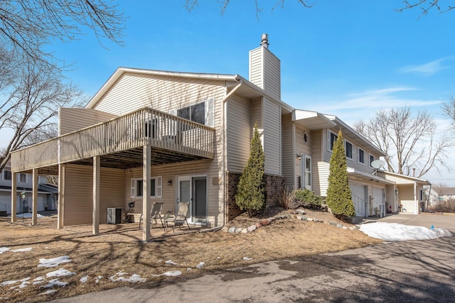 view of front facade featuring a patio, cooling unit, a wooden deck, a garage, and a chimney