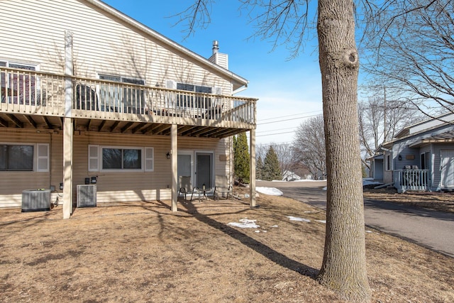 rear view of house with a wooden deck, cooling unit, and a chimney