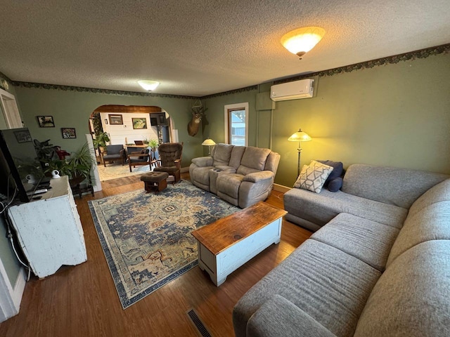 living area with a wall unit AC, wood finished floors, arched walkways, and a textured ceiling