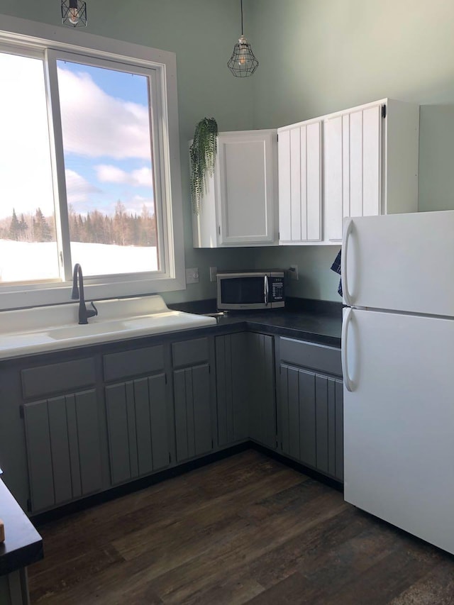 kitchen featuring dark countertops, stainless steel microwave, dark wood-style flooring, freestanding refrigerator, and a sink