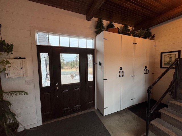 foyer featuring stairs, wood ceiling, concrete flooring, wood walls, and beamed ceiling