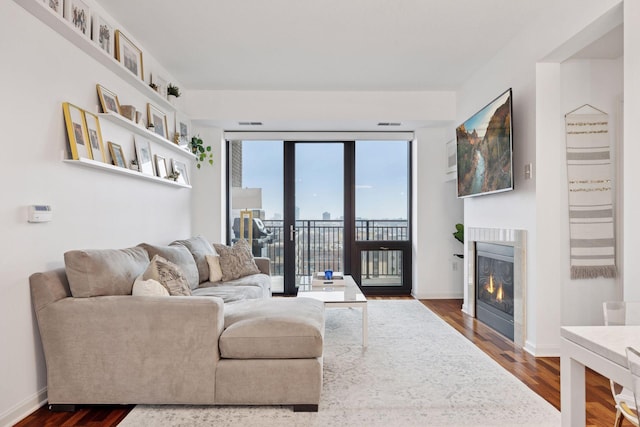 living room featuring a glass covered fireplace, visible vents, dark wood finished floors, and baseboards