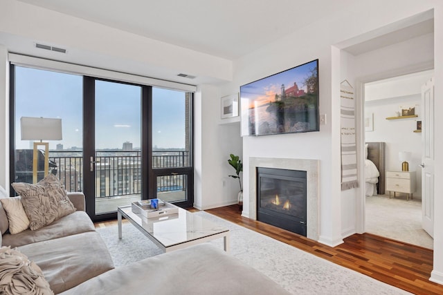 living room with a glass covered fireplace, visible vents, baseboards, and wood finished floors