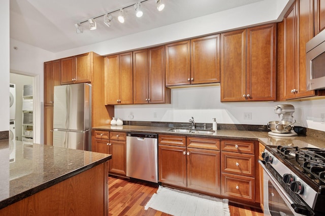 500 Grant St Unit 807, Minneapolis, MN 55404 - kitchen featuring light wood finished floors, dark stone counters, stacked washer and clothes dryer, appliances with stainless steel finishes, and a sink