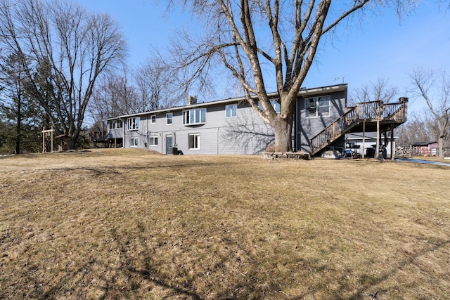 rear view of house featuring a wooden deck, stairway, a lawn, and a chimney