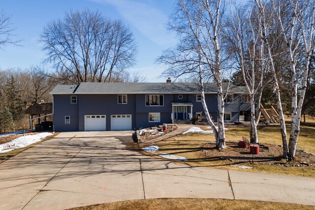 bi-level home with stairs, a chimney, concrete driveway, and an attached garage