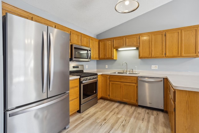 kitchen featuring light countertops, vaulted ceiling, light wood-style floors, stainless steel appliances, and a sink