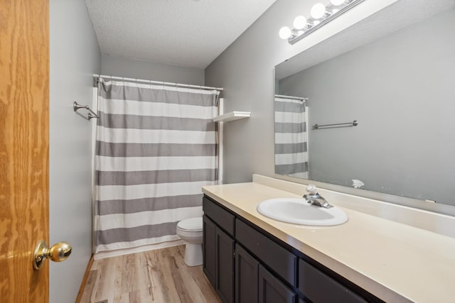 full bath with toilet, a shower with shower curtain, vanity, wood finished floors, and a textured ceiling