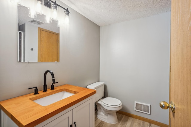 bathroom with vanity, wood finished floors, visible vents, a textured ceiling, and toilet