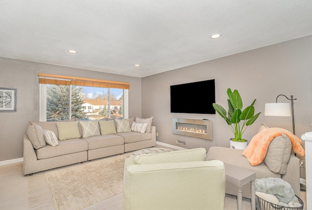 living area with a glass covered fireplace, recessed lighting, light wood-type flooring, and baseboards