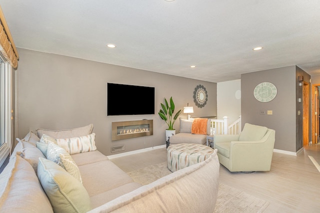 living room with a glass covered fireplace, recessed lighting, baseboards, and light wood-style floors