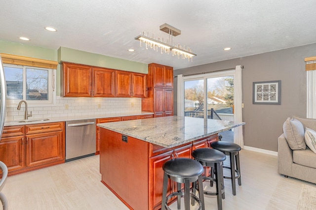 kitchen featuring light stone countertops, a sink, decorative backsplash, stainless steel dishwasher, and a kitchen breakfast bar