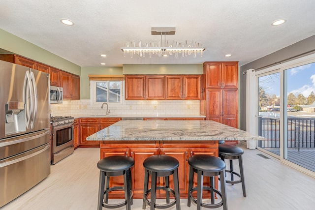 kitchen with a kitchen island, a breakfast bar, light stone counters, stainless steel appliances, and a sink