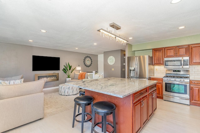 kitchen featuring a breakfast bar, tasteful backsplash, a center island, appliances with stainless steel finishes, and light stone countertops