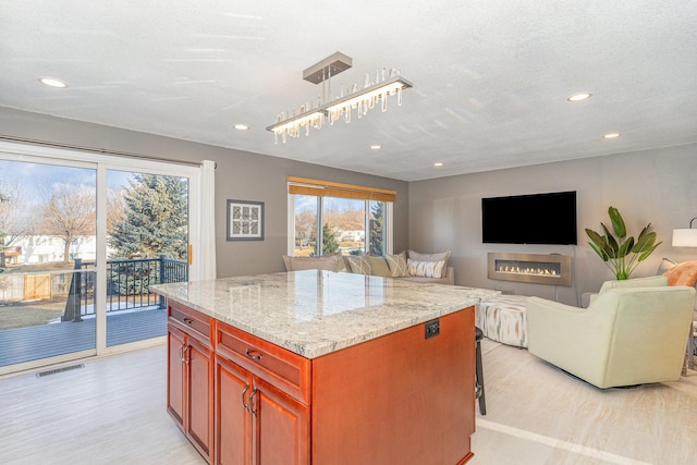 kitchen featuring light stone countertops, visible vents, light wood finished floors, a kitchen island, and open floor plan