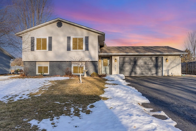 split level home with aphalt driveway, a garage, and fence