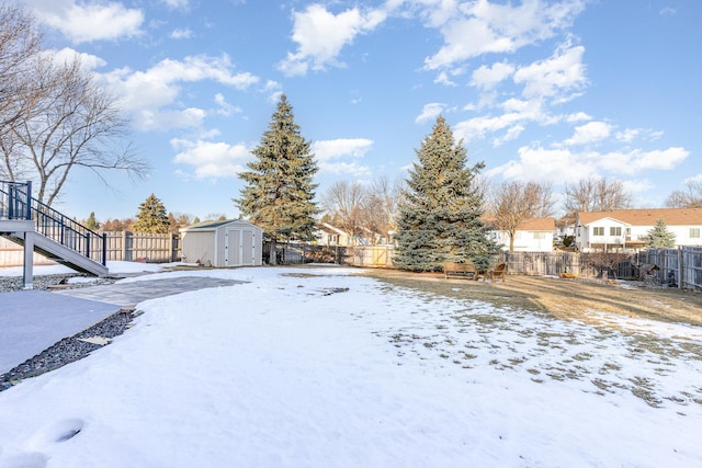 snowy yard with a residential view, an outbuilding, a fenced backyard, and a shed